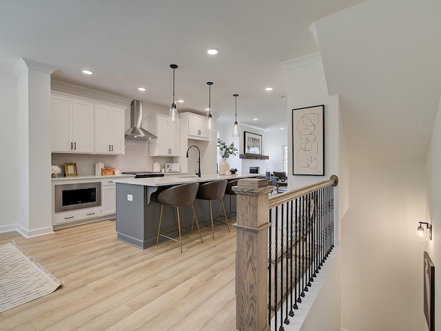 kitchen with wall chimney range hood, white cabinets, hanging light fixtures, and built in microwave