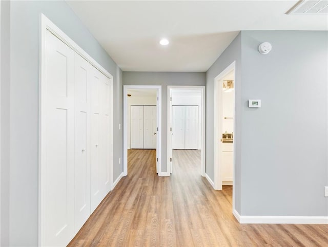 corridor featuring light wood finished floors, baseboards, and visible vents