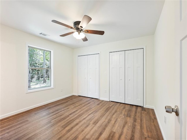 unfurnished bedroom featuring visible vents, baseboards, two closets, and wood finished floors