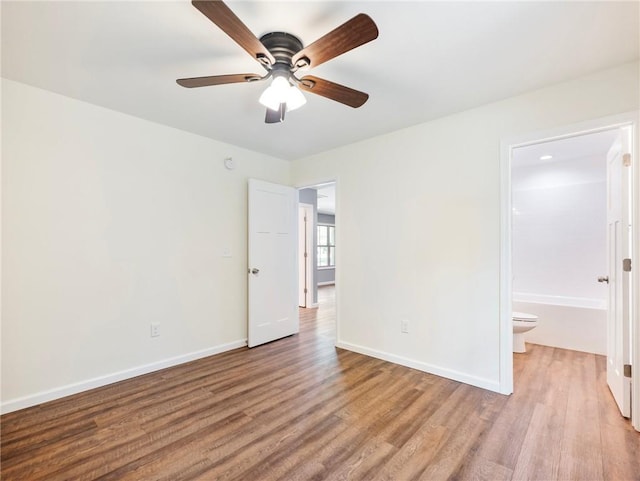 unfurnished bedroom featuring a ceiling fan, ensuite bath, baseboards, and wood finished floors