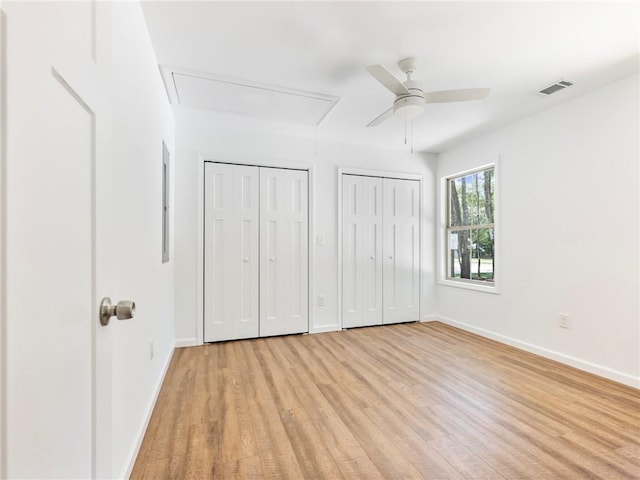 unfurnished bedroom featuring visible vents, baseboards, light wood finished floors, two closets, and attic access