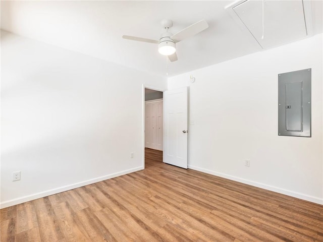 spare room featuring attic access, electric panel, baseboards, ceiling fan, and light wood-style floors