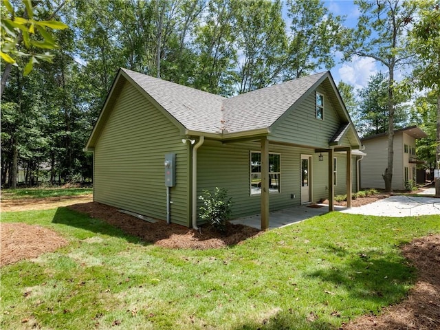 view of home's exterior with roof with shingles, a lawn, and a patio