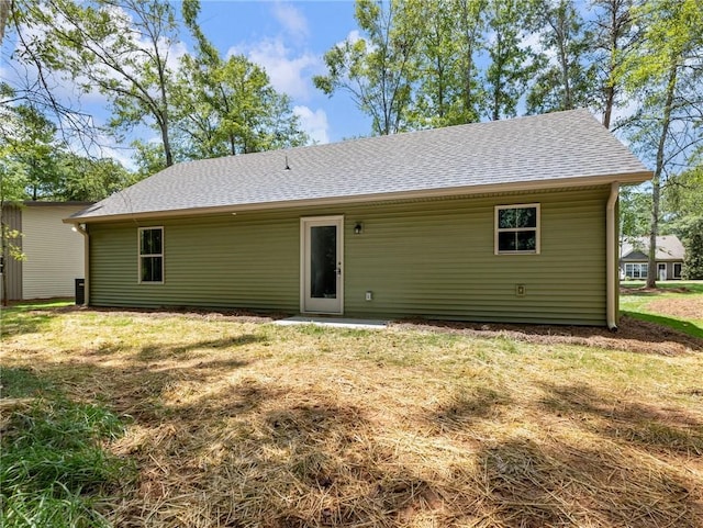 rear view of house with roof with shingles and a lawn