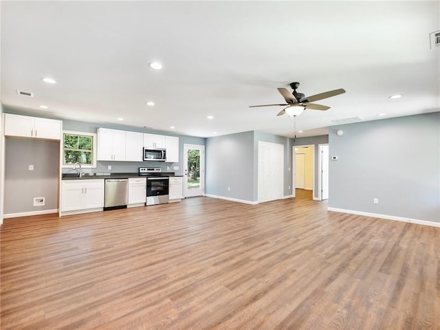 kitchen with appliances with stainless steel finishes, light wood-type flooring, open floor plan, and white cabinetry