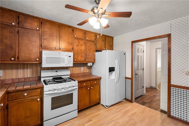 2617 Laurel Woods Ln SE, Conyers, GA 30094 - kitchen featuring white appliances, wallpapered walls, tile countertops, ceiling fan, and brown cabinetry