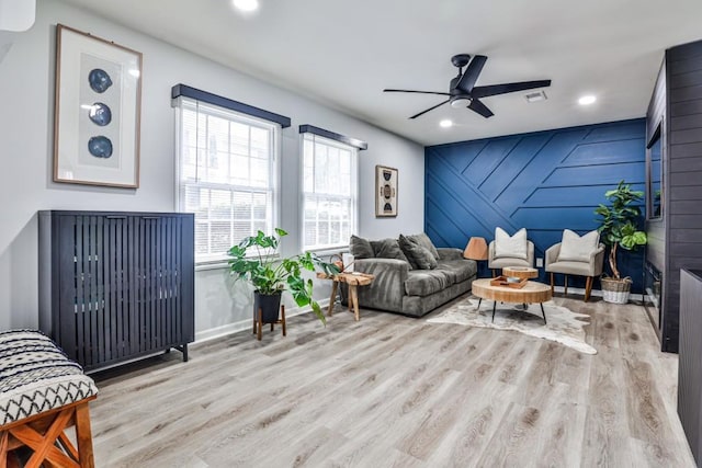 living room featuring ceiling fan, light hardwood / wood-style floors, and wood walls