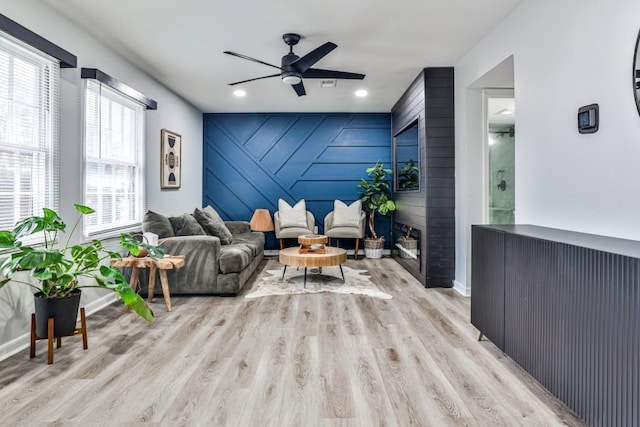 living room with wooden walls, ceiling fan, a fireplace, and light wood-type flooring