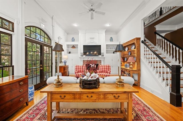 living room with french doors, built in shelves, ceiling fan, light wood-type flooring, and ornamental molding