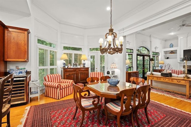 dining space with french doors, ceiling fan with notable chandelier, crown molding, built in shelves, and light wood-type flooring