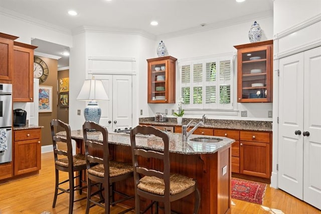 kitchen with a center island with sink, light hardwood / wood-style flooring, ornamental molding, stone countertops, and a breakfast bar area