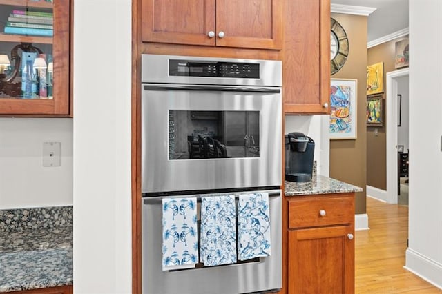 kitchen featuring light stone countertops, crown molding, stainless steel double oven, and light wood-type flooring