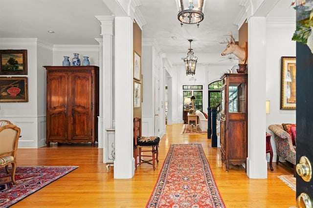 corridor with an inviting chandelier, light wood-type flooring, ornamental molding, and ornate columns