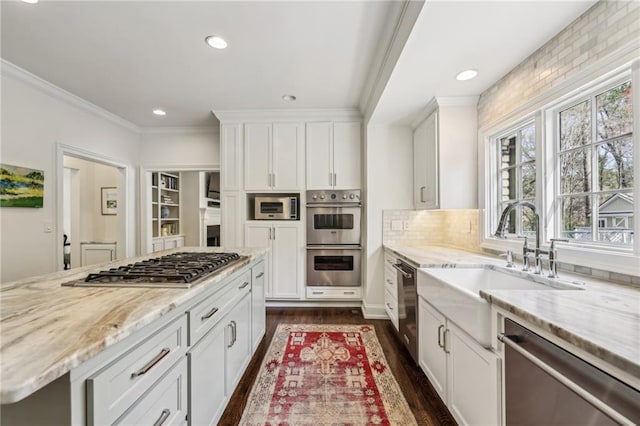 kitchen with stainless steel appliances, a sink, white cabinets, light stone countertops, and crown molding