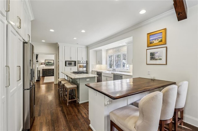 kitchen featuring appliances with stainless steel finishes, a breakfast bar, dark wood-style flooring, and ornamental molding