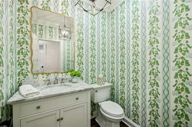 bathroom with a notable chandelier, vanity, toilet, and wallpapered walls