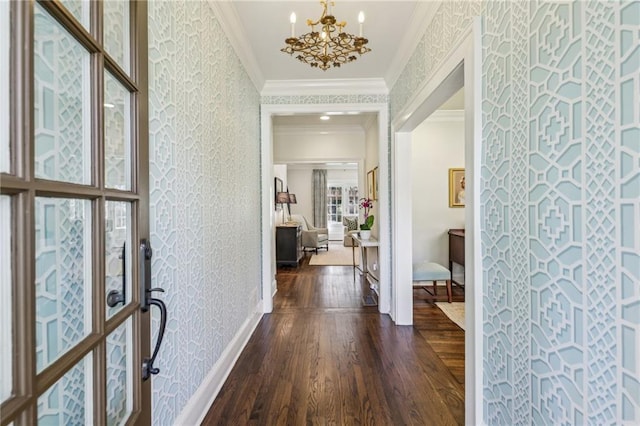 foyer with wallpapered walls, baseboards, ornamental molding, dark wood-type flooring, and a notable chandelier