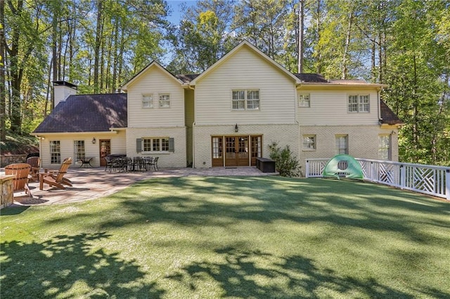 back of house featuring a patio, brick siding, fence, a yard, and a chimney