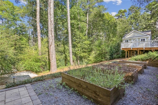 view of yard featuring a vegetable garden, a wooden deck, and a view of trees