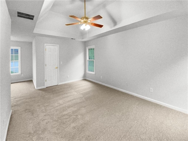 unfurnished bedroom with ceiling fan, carpet floors, a tray ceiling, and multiple windows