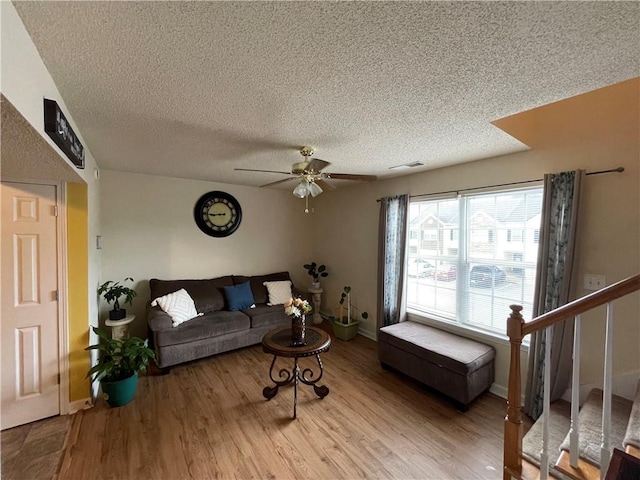 living room featuring light wood-type flooring, a textured ceiling, and ceiling fan