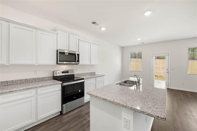 kitchen featuring sink, dark wood-type flooring, appliances with stainless steel finishes, white cabinetry, and a center island with sink