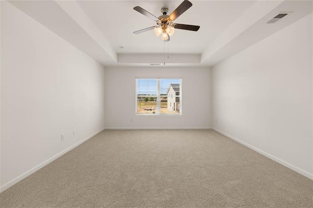 carpeted empty room with a raised ceiling and ceiling fan