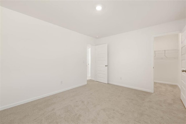 unfurnished bedroom featuring a walk in closet, light colored carpet, and a closet