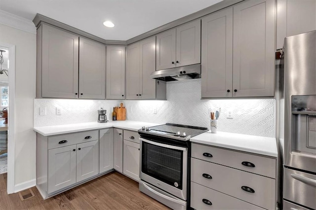 kitchen with wood finished floors, gray cabinetry, stainless steel appliances, light countertops, and under cabinet range hood