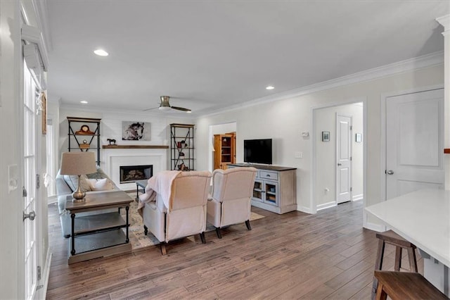 living area with a fireplace, crown molding, wood finished floors, and ceiling fan