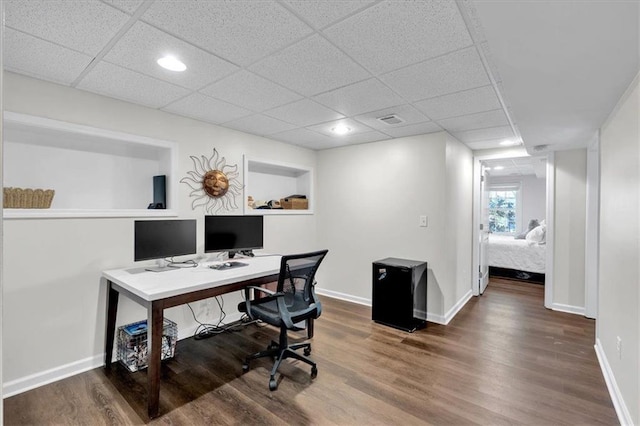 home office featuring visible vents, a drop ceiling, baseboards, and wood finished floors