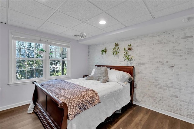 bedroom featuring dark wood finished floors, a drop ceiling, and baseboards