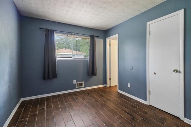 unfurnished bedroom with a textured ceiling and dark wood-type flooring