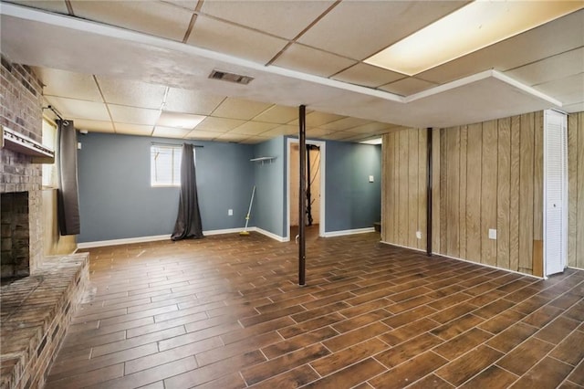 basement featuring a paneled ceiling, a fireplace, wooden walls, and dark hardwood / wood-style flooring