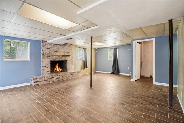 basement with dark hardwood / wood-style flooring, a brick fireplace, and a paneled ceiling