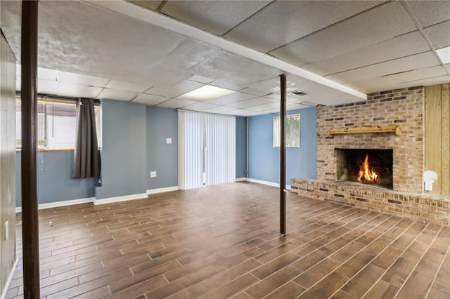 basement featuring a drop ceiling, dark hardwood / wood-style floors, a brick fireplace, and a wealth of natural light