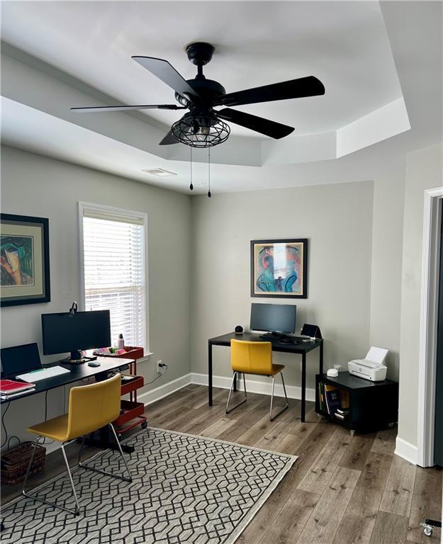 office space with wood-type flooring, a tray ceiling, and ceiling fan