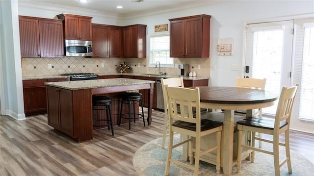 kitchen with ornamental molding, a kitchen island, hardwood / wood-style flooring, stainless steel appliances, and decorative backsplash