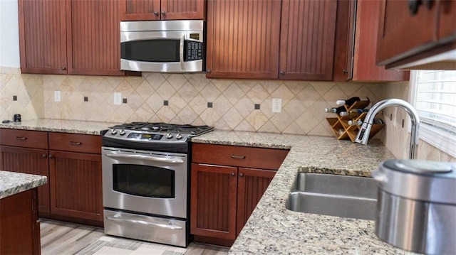 kitchen with light stone countertops, stainless steel appliances, tasteful backsplash, and light hardwood / wood-style flooring