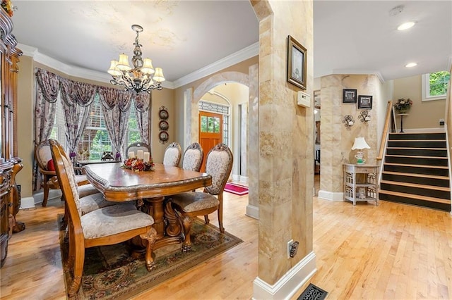 dining area featuring arched walkways, light wood-style flooring, ornamental molding, stairway, and an inviting chandelier