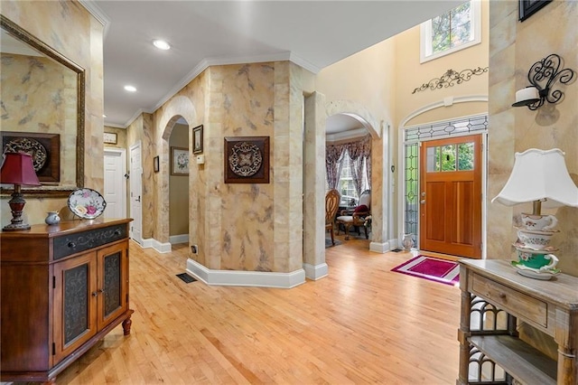 entryway with baseboards, light wood-style flooring, arched walkways, and crown molding