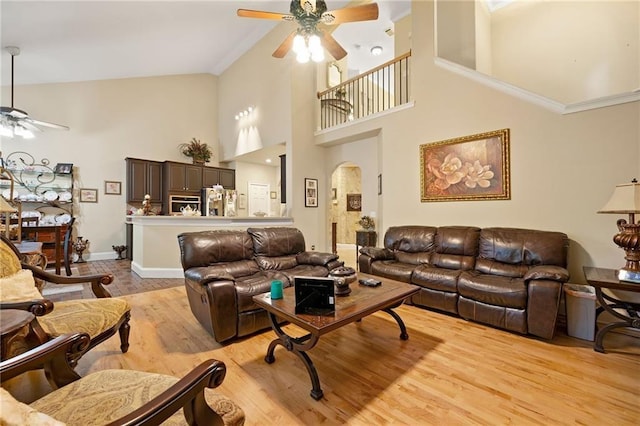 living room with a towering ceiling, light wood-style floors, ornamental molding, ceiling fan, and baseboards