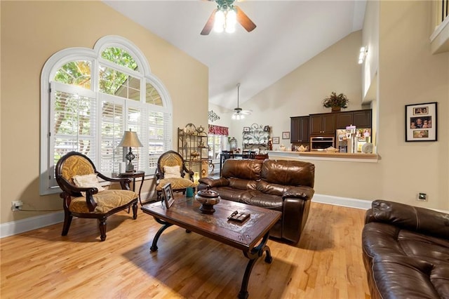 living room featuring a ceiling fan, high vaulted ceiling, light wood-style flooring, and baseboards