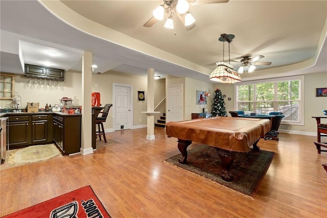 game room featuring light wood-style flooring, wet bar, baseboards, and a raised ceiling