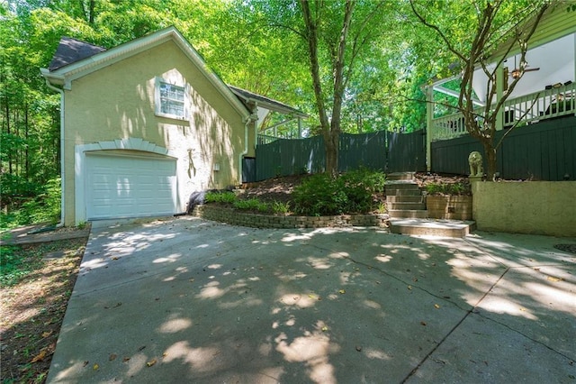 view of side of property featuring an attached garage, fence, concrete driveway, and stucco siding