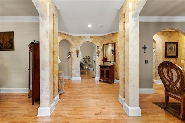 hall with light wood-style floors, baseboards, arched walkways, and crown molding