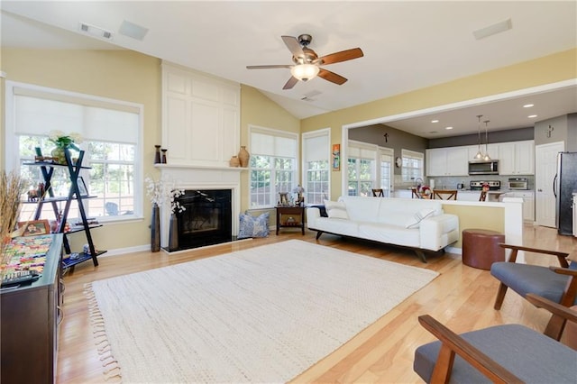 living area with lofted ceiling, a large fireplace, visible vents, and light wood-style floors