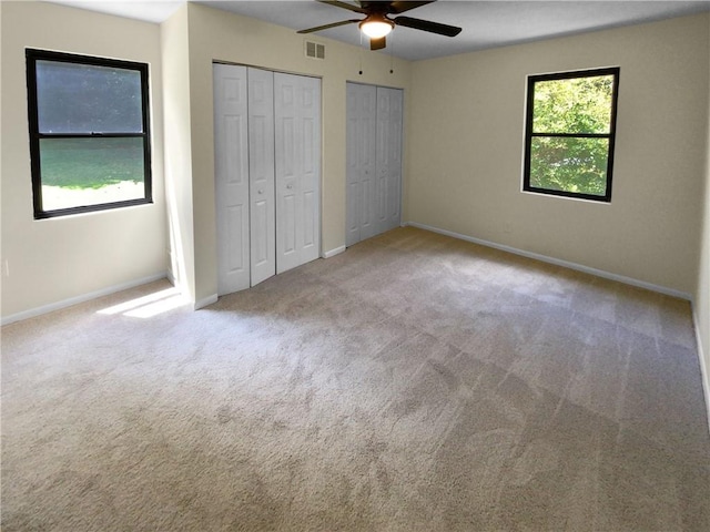 unfurnished bedroom featuring light colored carpet, multiple closets, multiple windows, and ceiling fan