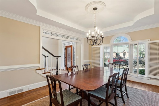 dining area with hardwood / wood-style flooring, ornamental molding, a raised ceiling, and an inviting chandelier