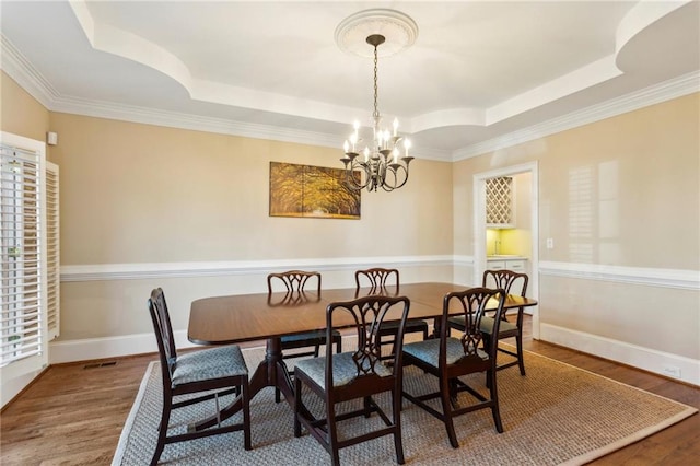 dining room with an inviting chandelier, hardwood / wood-style floors, and a raised ceiling